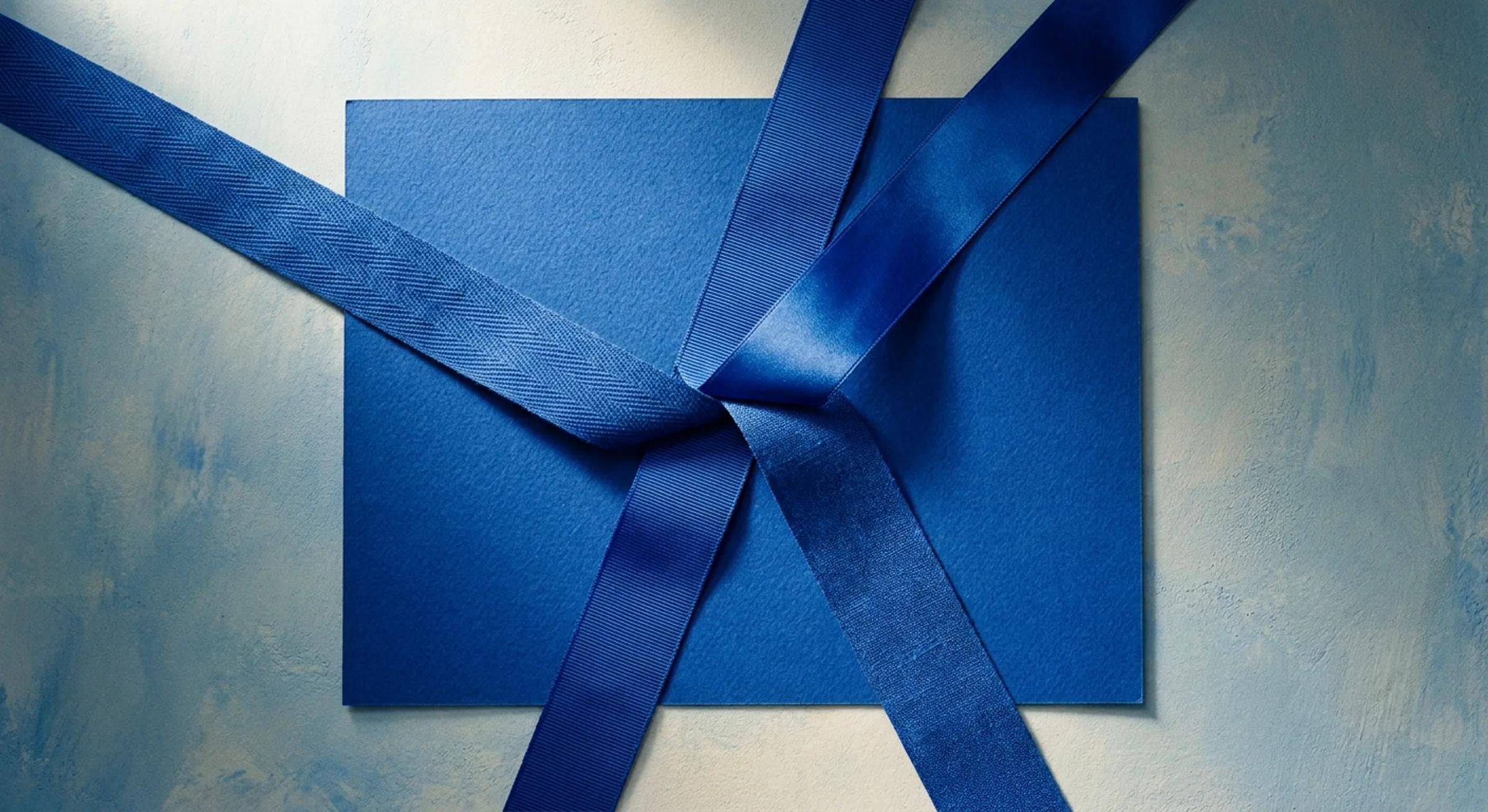 Four ribbons of cobalt fabric, each a different weave, lying across one shared sheet of paper and overlapping where they meet at the centre.